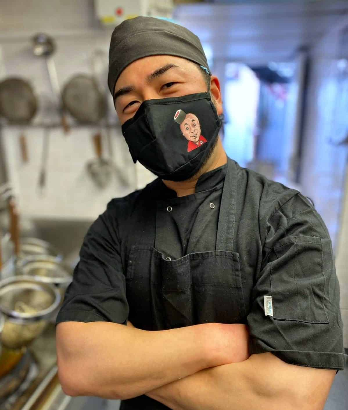 key to producing great sushi near me are talented sushi chefs, this is a picture of a Tenkaichi chef with his arms crossed and wearing a Tenkaichi branded face mask