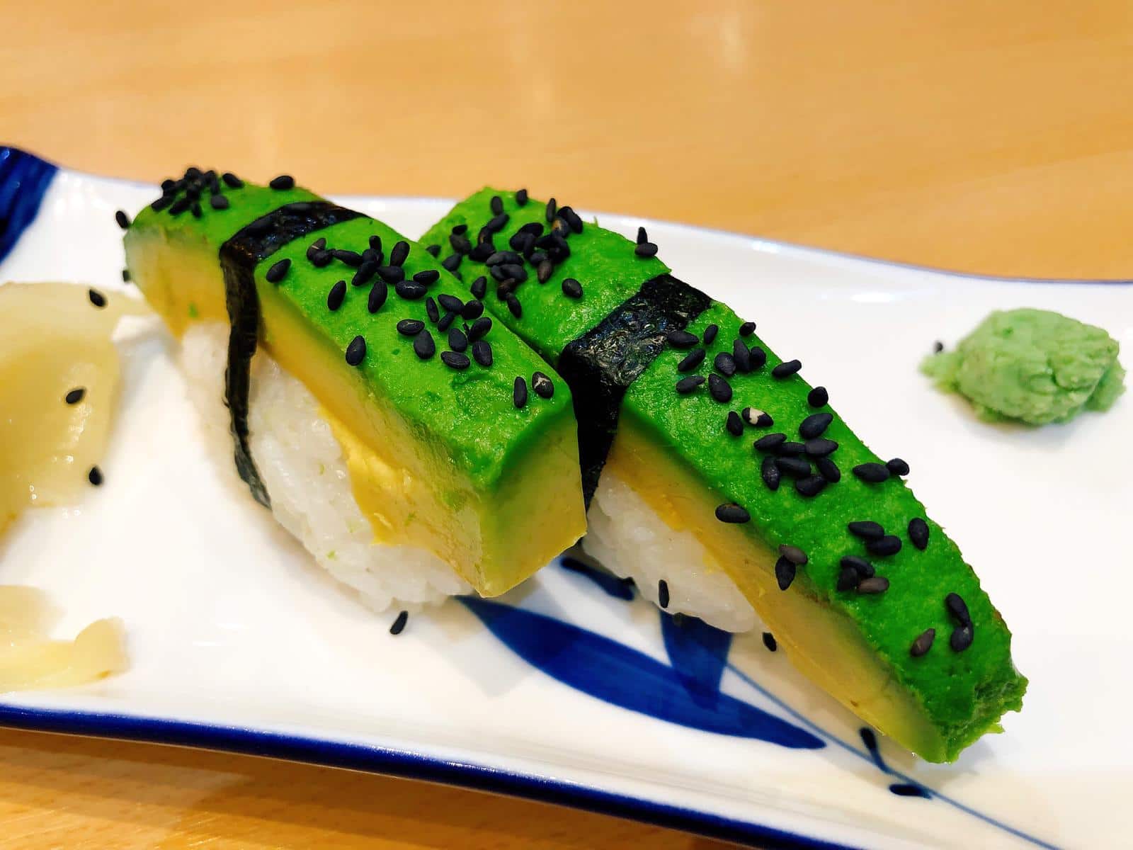 Two pieces of Avocado Nigiri with wasabi and ginger arranged on a blue and white plate. Part of the Tenkaichi Vegan Sushi range